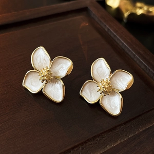 Elegante Ohrstecker mit weißen Emaille-Blumen und Vergoldung auf Holztablett