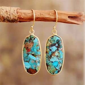 Detail of bohemian gold-rimmed teardrop earrings with blue imperial stone on wood