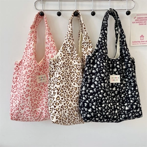Detailed close-up of three leopard print canvas tote bags with heart patterns and woven labels