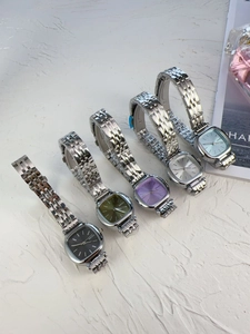 Five elegant women's square watches with colored dials and silver steel bands on a magazine