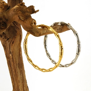 Detail view of bamboo-shaped titanium steel bangles in gold and silver on a wooden stand