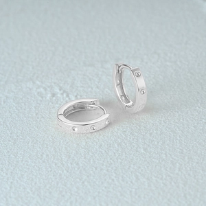 Detail shot of silver square hoop earrings with textured dotted patterns on light blue background