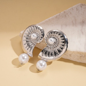 Macro detail of silver shell earrings with pearls against a textured stone background