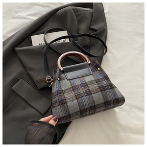 Detail of plaid tweed handbag with wooden handle and gold hardware on grey blazer