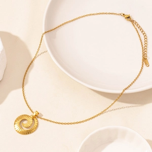Detailed view of a gold spiral disc pendant necklace on elegant ceramic tray