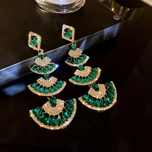 Detailed close-up of emerald and gold fan-shaped drop earrings with sparkling rhinestones