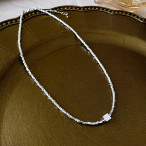 Detail of silver irregular beads necklace with a minimalist cube pendant on vintage tray