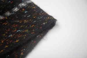 Detailed macro view of black knit fabric with colorful flecks and patterned woven edges