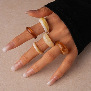 Detailed view of colorful acrylic resin geometric rings worn on fingers with a warm aesthetic
