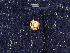 Dettaglio macro del tessuto tweed blu scuro con paillettes dorate e bottone a spirale