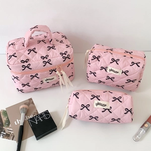 Three-piece pink quilted makeup bag set featuring elegant black bow patterns and ribbons