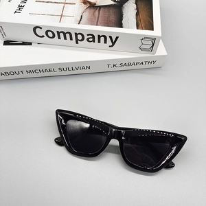 Close-up of retro black cat-eye sunglasses placed below minimalist white books