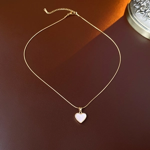 Gros plan d'un collier cœur doré en titane avec nacre blanche sur fond de cuir