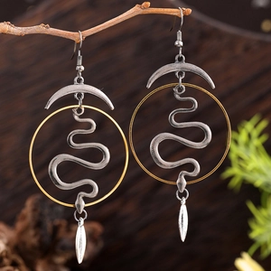 Close-up of gothic snake and crescent moon earrings hanging on a natural tree branch