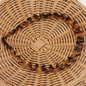 Detail shot of a tortoiseshell wave headband placed on a woven rattan mat background