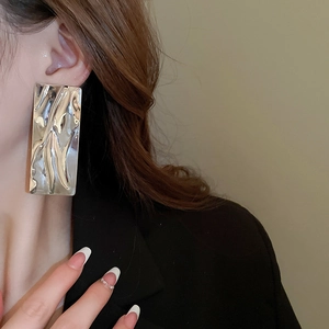 Detail of a model wearing silver rectangular earrings with a liquid metal texture