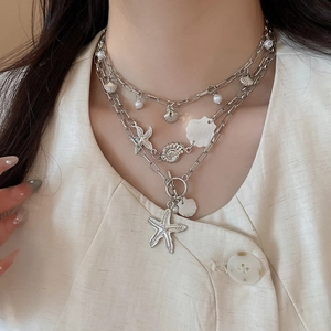 Close-up of layered bohemian necklace featuring starfish, sea shells and pearls on a model