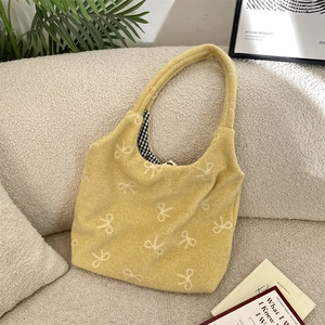 Sac fourre-tout en peluche jaune à motif de nœud blanc sur un canapé, style épuré