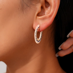 Close-up of geometric C-shaped enamel earrings with wavy patterns worn on a model's ear