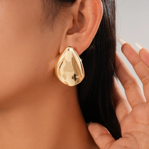 Close-up of metallic golden leaf-shaped earrings on model for a modern minimalist look