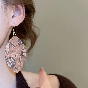 Detailed close-up of leaf-shaped cork earrings with vintage prints on a model