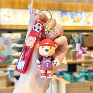 Close-up of a cartoon bear football mascot keychain with red silicone strap and soccer ball