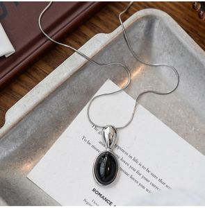 Detailed close-up of a silver snake chain necklace with an oval black resin stone pendant