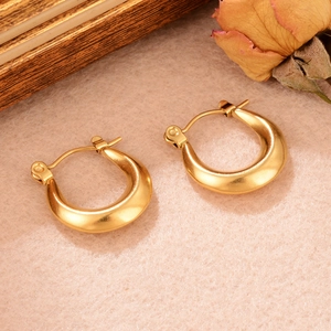 Gros plan de boucles d'oreilles créoles dorées épaisses avec texture sur fond rose