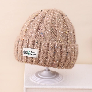Detail of beige knit beanie showing multi-color speckles and a smile graphic patch