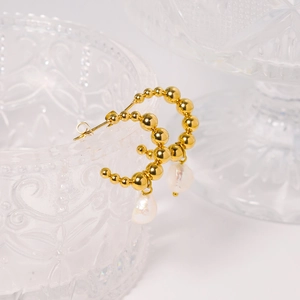 Golden beaded C-shaped hoop earrings with baroque pearl drop on textured glass