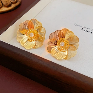 Detailed close-up of gold hollow flower stud earrings with sparkling rhinestone center
