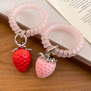 Détail de chouchous spirales roses avec breloques fraises en peluche sur livre ancien