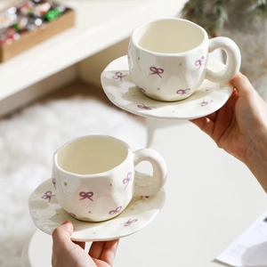 Detail of two cream ceramic coffee cups with purple bows and irregular handles