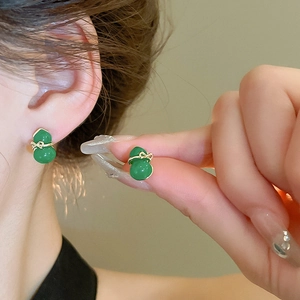 Detailed close-up of emerald green gourd earrings with gold bow accents on a model
