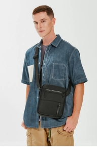 Detail of a black waterproof nylon crossbody bag worn by a model in a studio setting