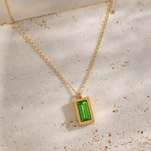 Close-up of gold chain necklace with a green emerald-cut zircon pendant on beige stone