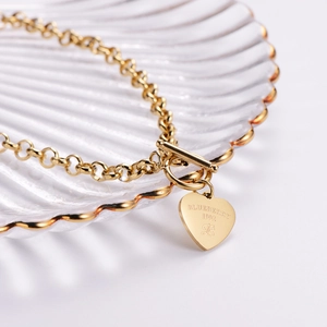 Elegant gold heart pendant bracelet with T-bar clasp on a luxury shell texture display tray