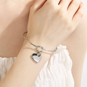 Polished silver stainless steel open bangle with a heart charm shown on a model wrist