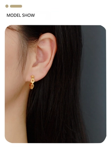 Close-up of a gold chain link earring with red accents worn by a model in a side profile