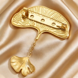 Macro shot of gold ginkgo leaf brooch with chain on champagne silk fabric background