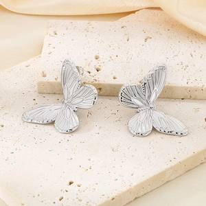 Macro detail of silver butterfly earrings with fine texture on beige silk fabric
