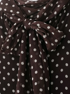 Dettaglio di una camicetta marrone a pois con un grande ed elegante fiocco al collo