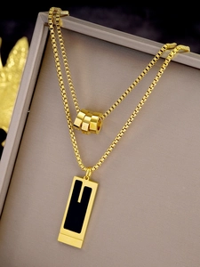 Detail of double-layer gold necklace with cylinder beads and geometric pendant on jewelry box