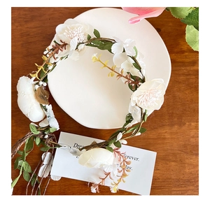 Close-up of white silk flowers and green leaves on a rustic vine crown headband