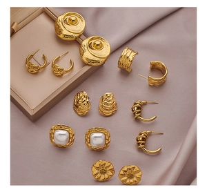 Macro shot of gold stainless steel pearl earrings and sunflower spiral studs on silk
