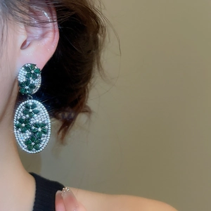 Close-up of vintage oval drop earrings with green and white zircons worn on ear