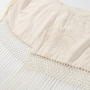 Détail du châle en satin beige avec broderie florale élégante et finitions à franges