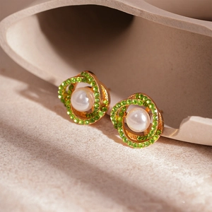 Elegant gold spiral stud earrings with green rhinestones and white pearls on stone tray
