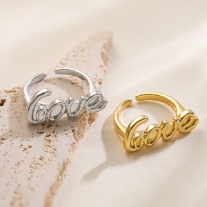 Minimalist gold and silver Love open rings displayed on a natural textured stone base