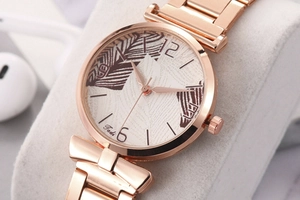Macro shot of rose gold mesh watch with leaf pattern dial and metal strap details